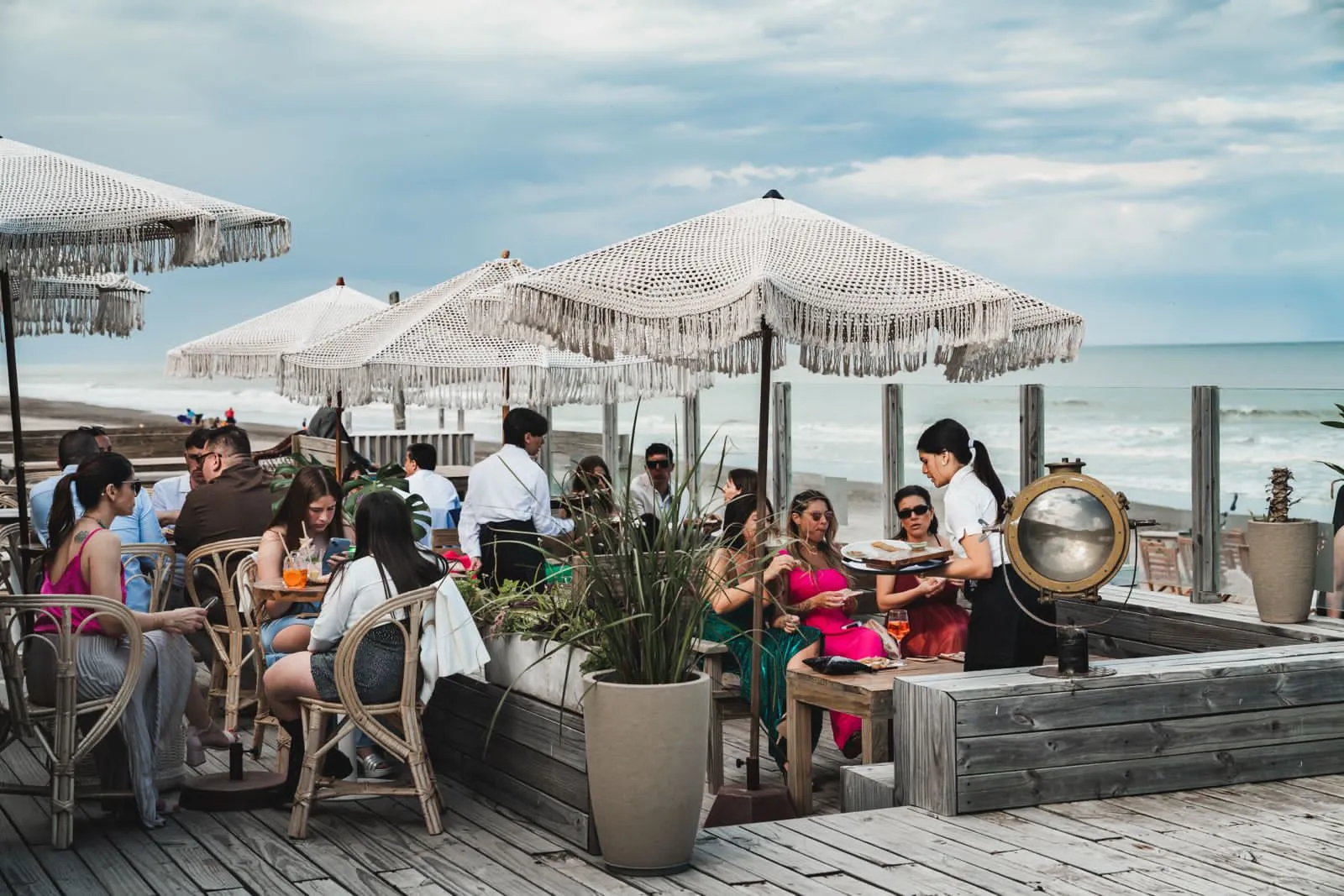 Invitados en las mesas del deck, bajo las sombrillas de flecos y frente al mar