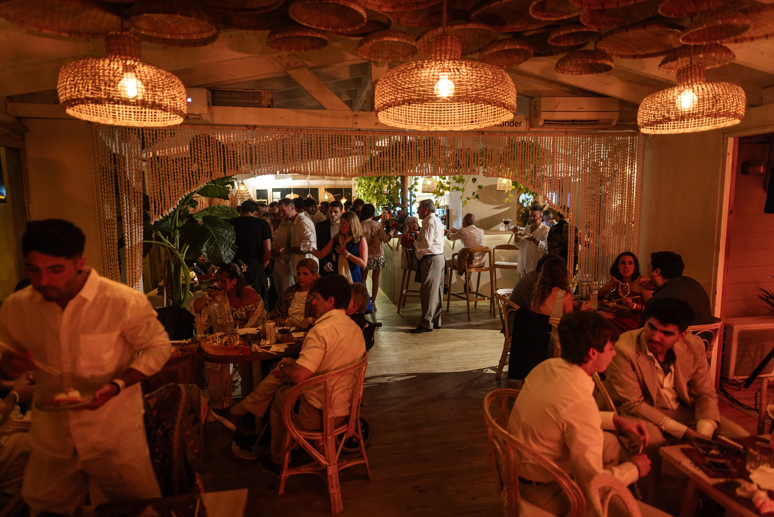 Invitados cenando en el salón, bajo las lámparas de fibra natural