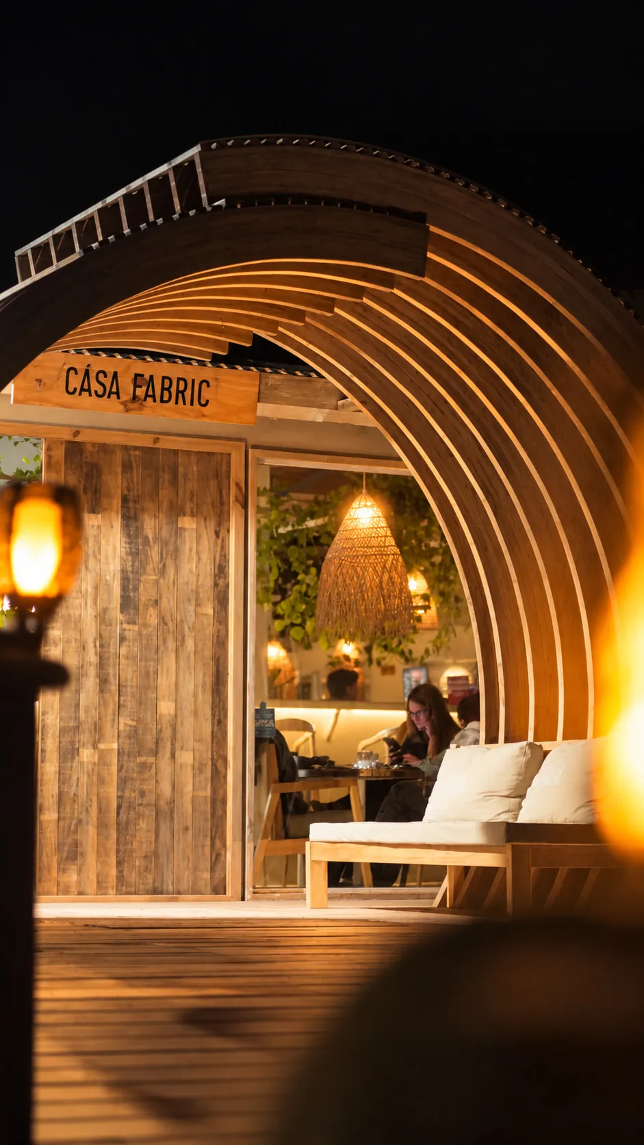 El túnel de madera curvo de la entrada a Casa Fabric, iluminado de noche